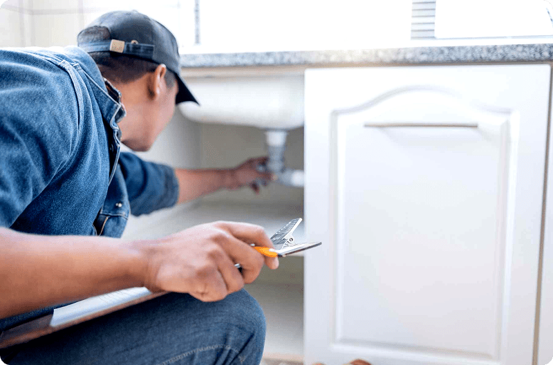 A man fixing plumbing under a kitchen sink with tools.