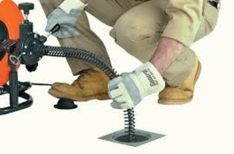 Person using a tool to unclog a drain with protective gloves.