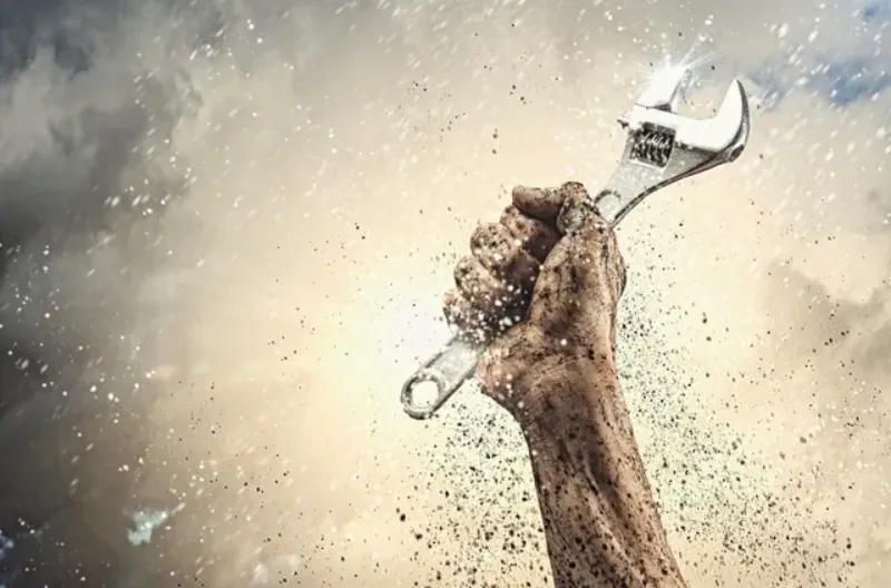 A clenched fist holding a wrench, dissolving into particles.