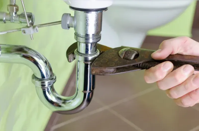 Hand using a wrench to fix a sink pipe under a bathroom sink.